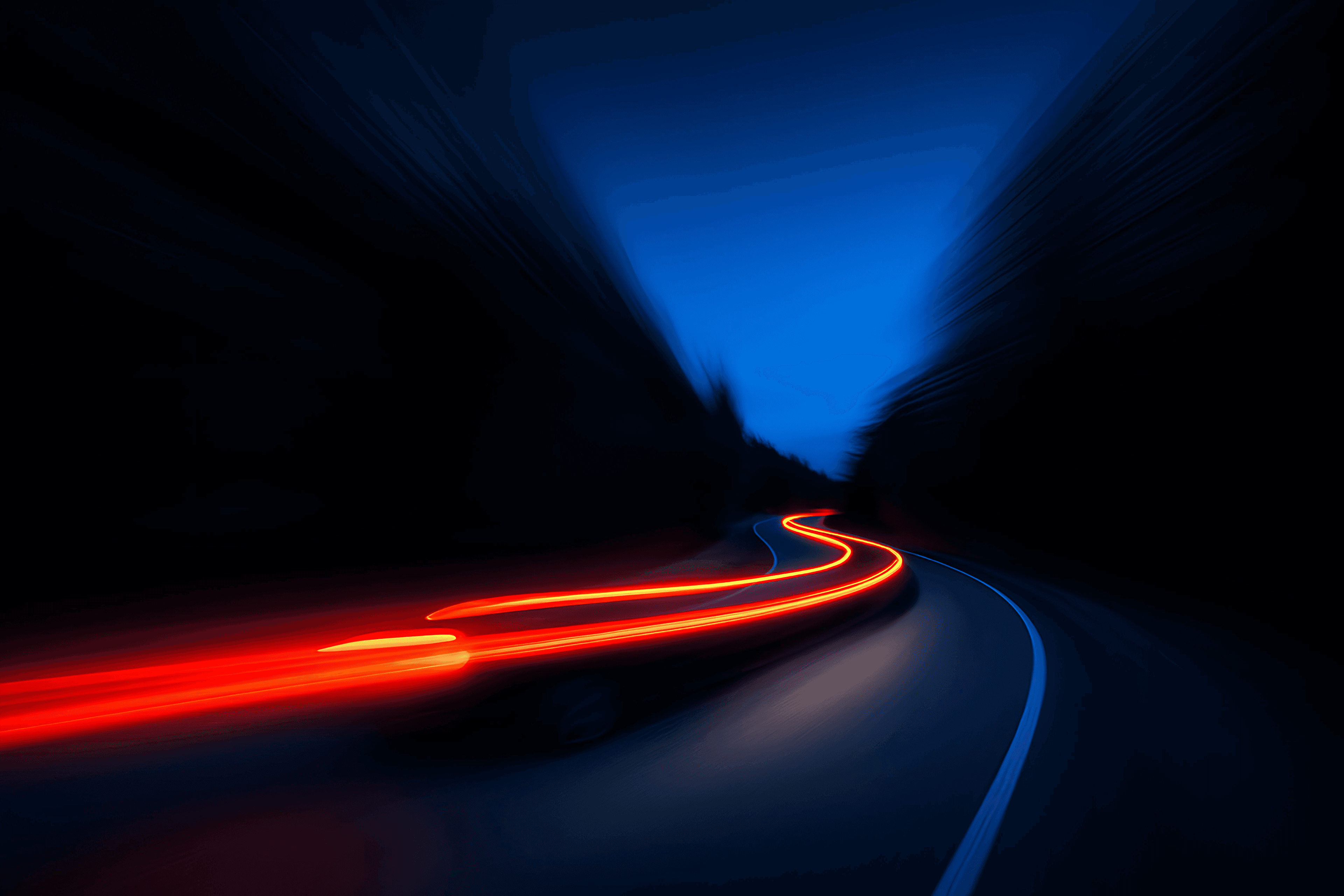 Long exposure shot of a car's red taillights creating bright, wavy light trails on a dark, winding road at night, with blurred dark trees on either side and a deep blue sky above, conveying a sense of speed.